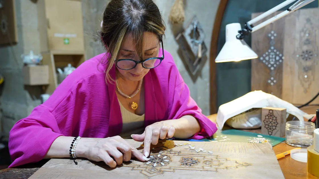 Manos trabajando un motivo de marquetería con piezas de chapa de distintas maderas sobre la mesa del taller